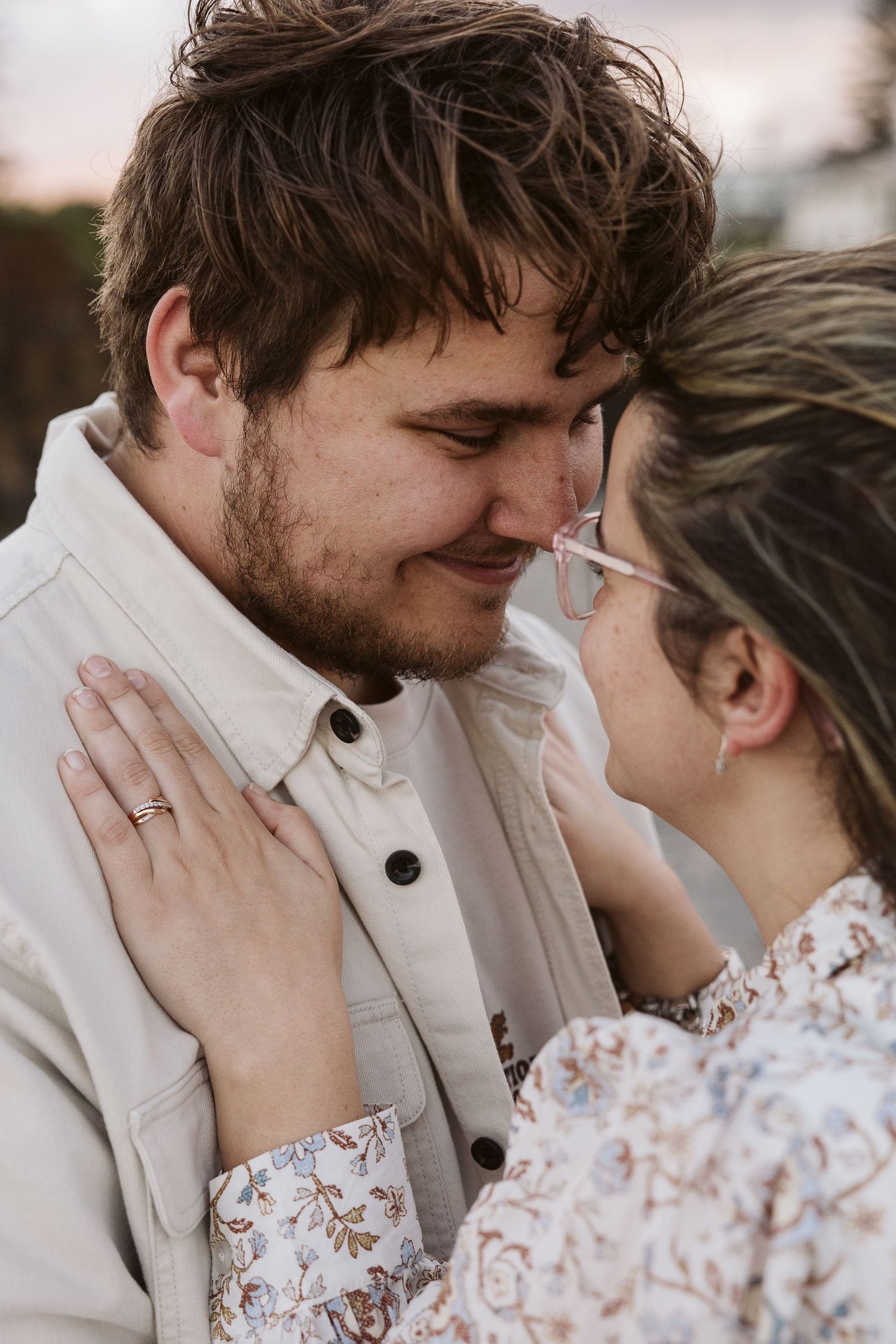 Romantic couple almost kissing with foreheads together, woman in floral dress placing hand on mans chest.
