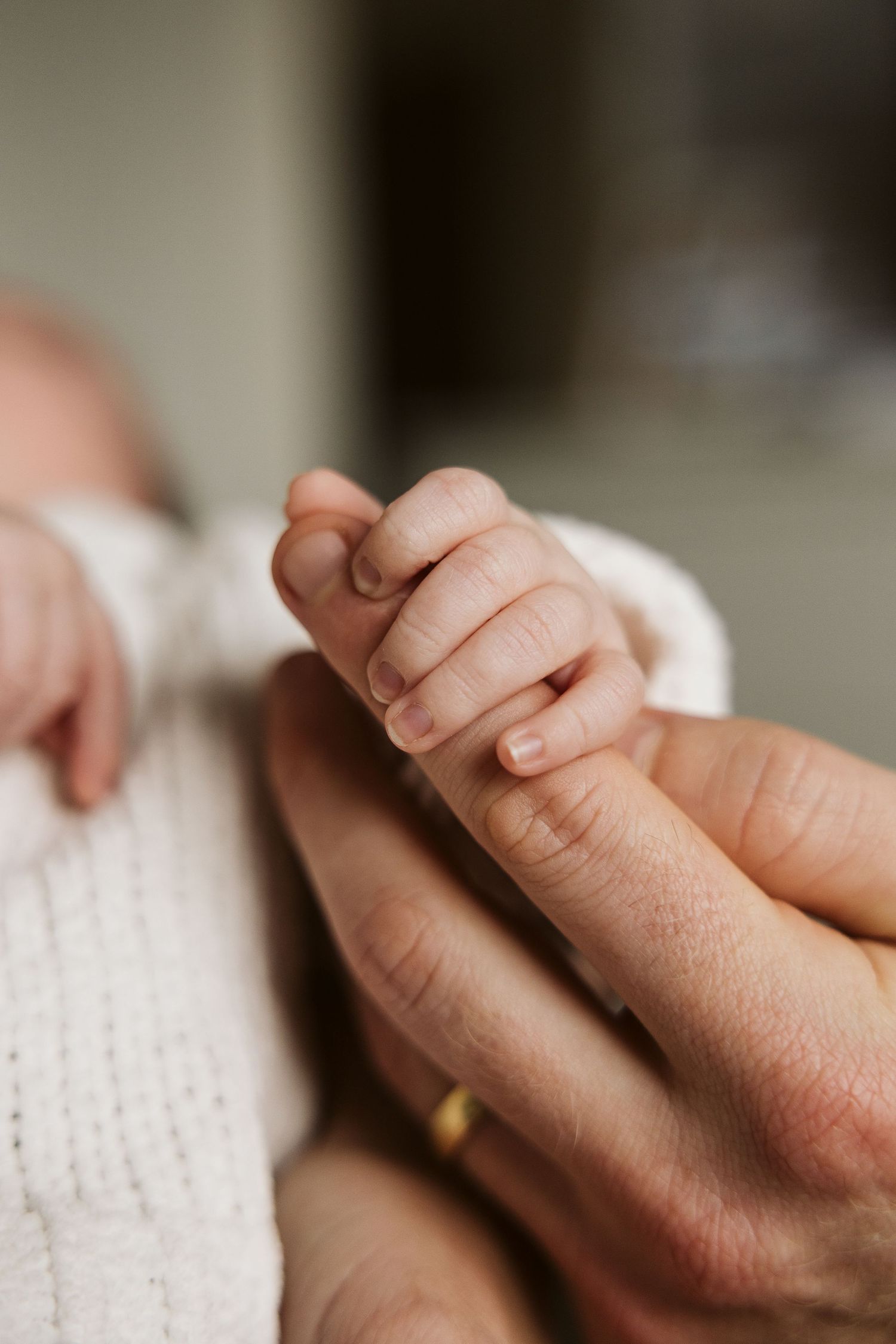 Newborn baby's tiny hand gripping parent's finger with gold wedding band.