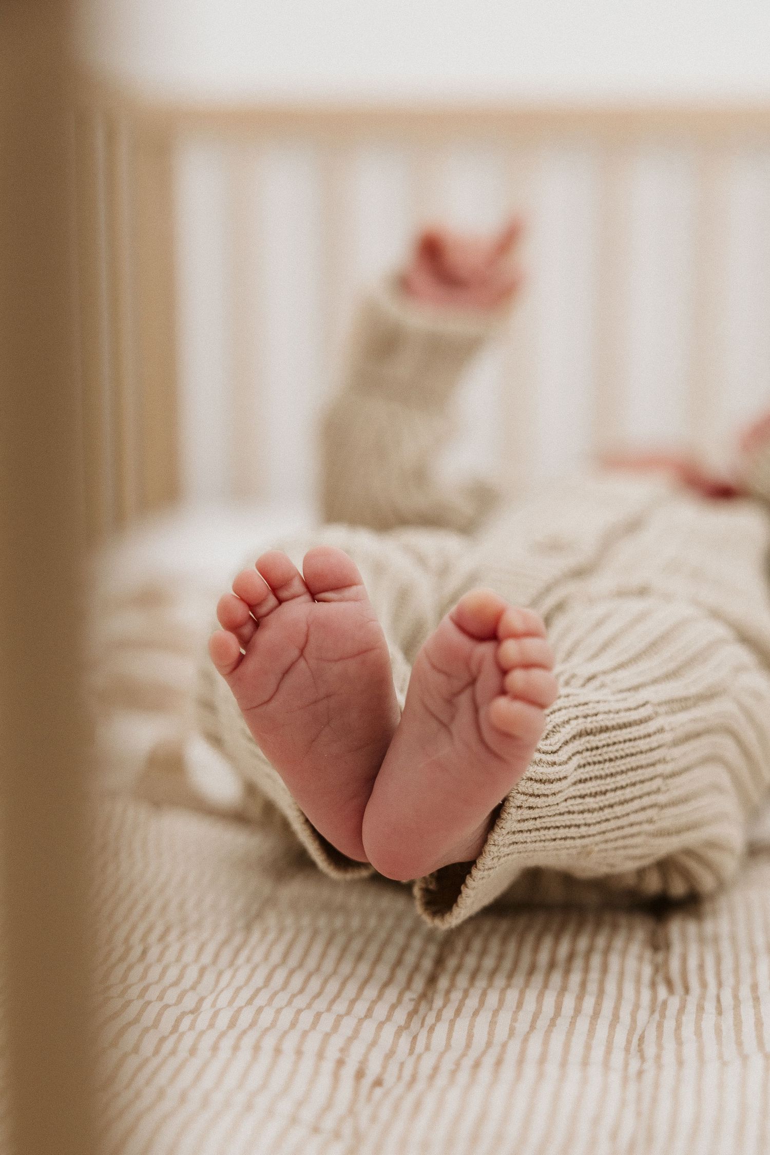 Close-up of newborn baby feet in a cream knit onesie lying in a wooden crib.