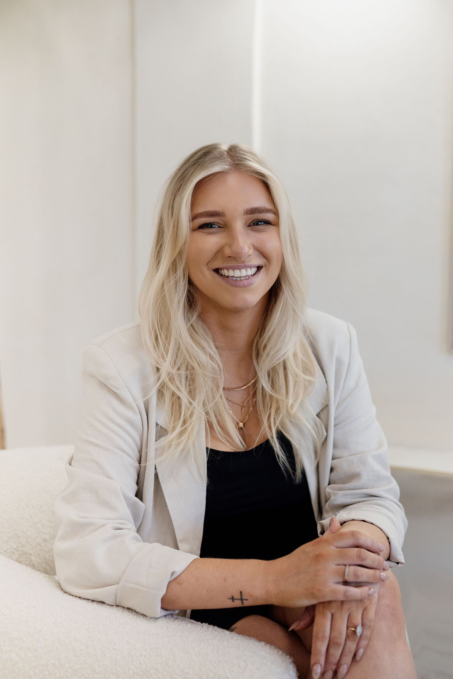 Smiling blonde woman in a white blazer sitting in a modern bright interior space.