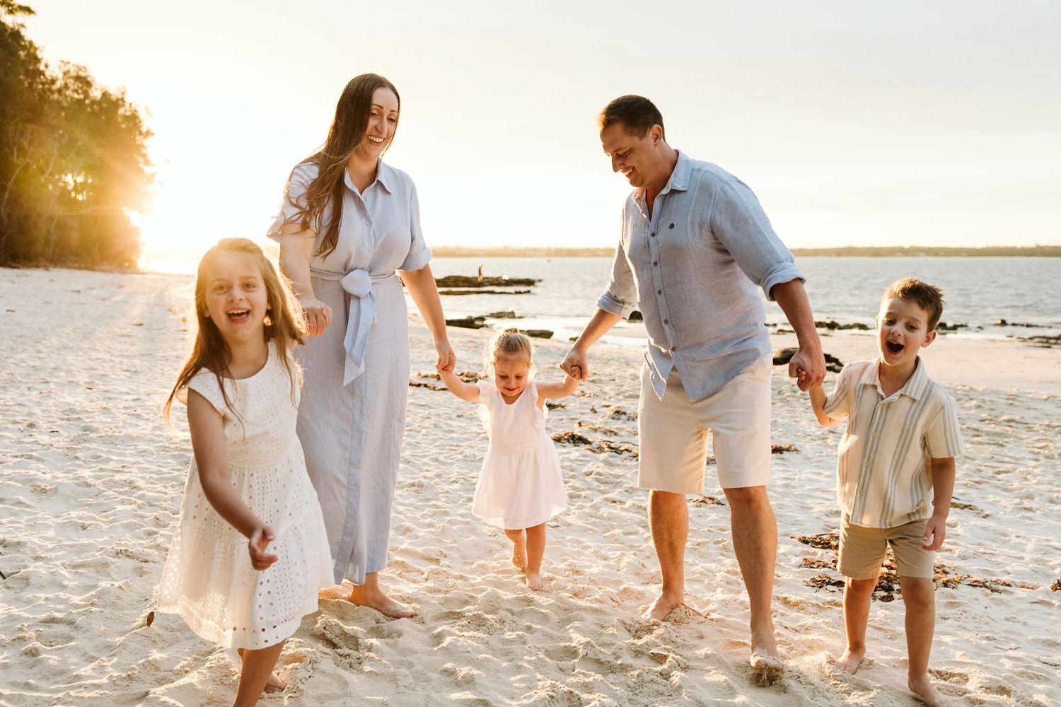 Joyful family of five walking on a sunny beach at golden hour, children laughing and playing.