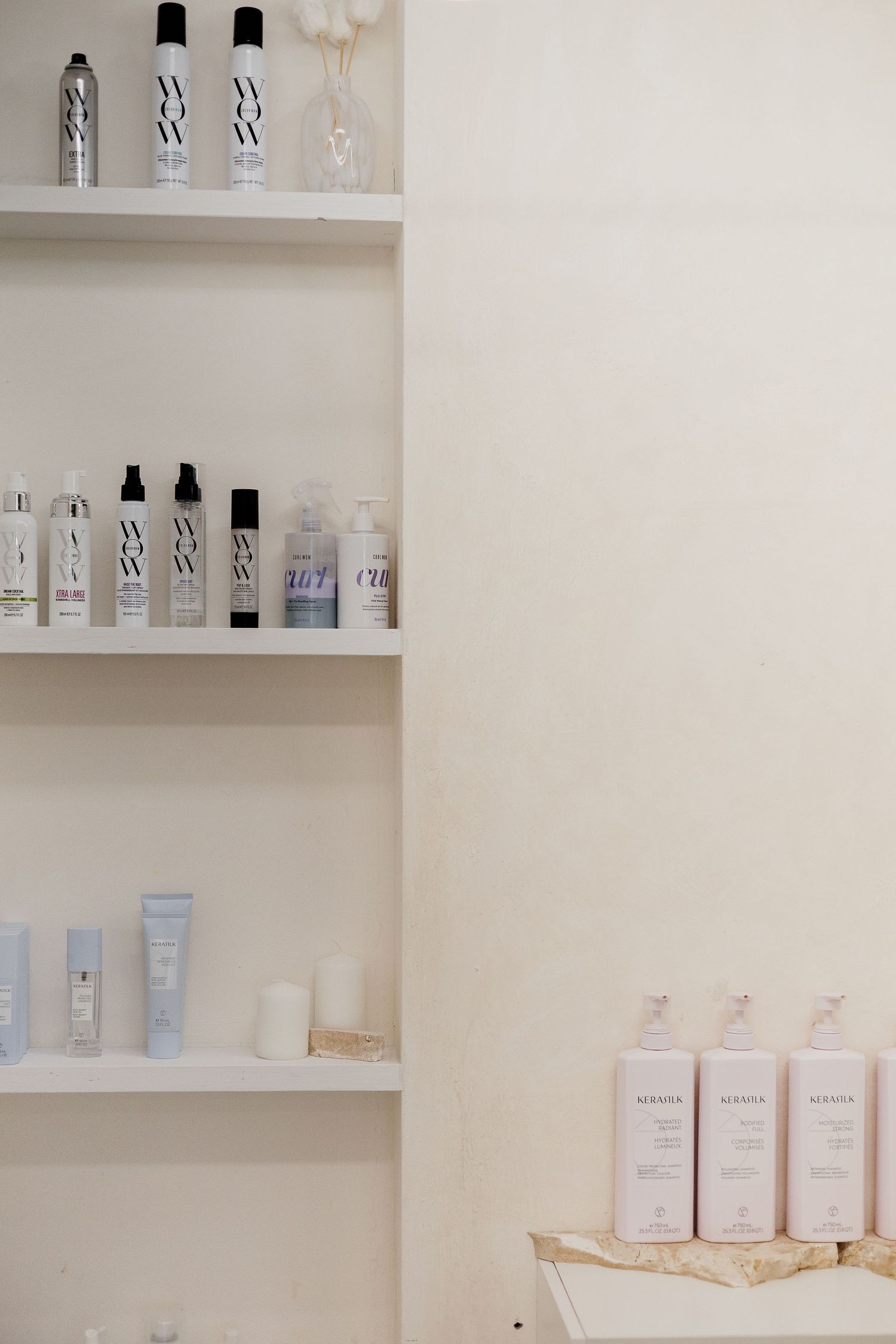 Hair care products displayed on white shelves in a minimalist beauty salon retail area.