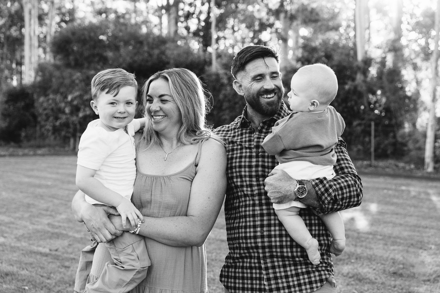 Black and white portrait of family of four with two young boys outdoors.