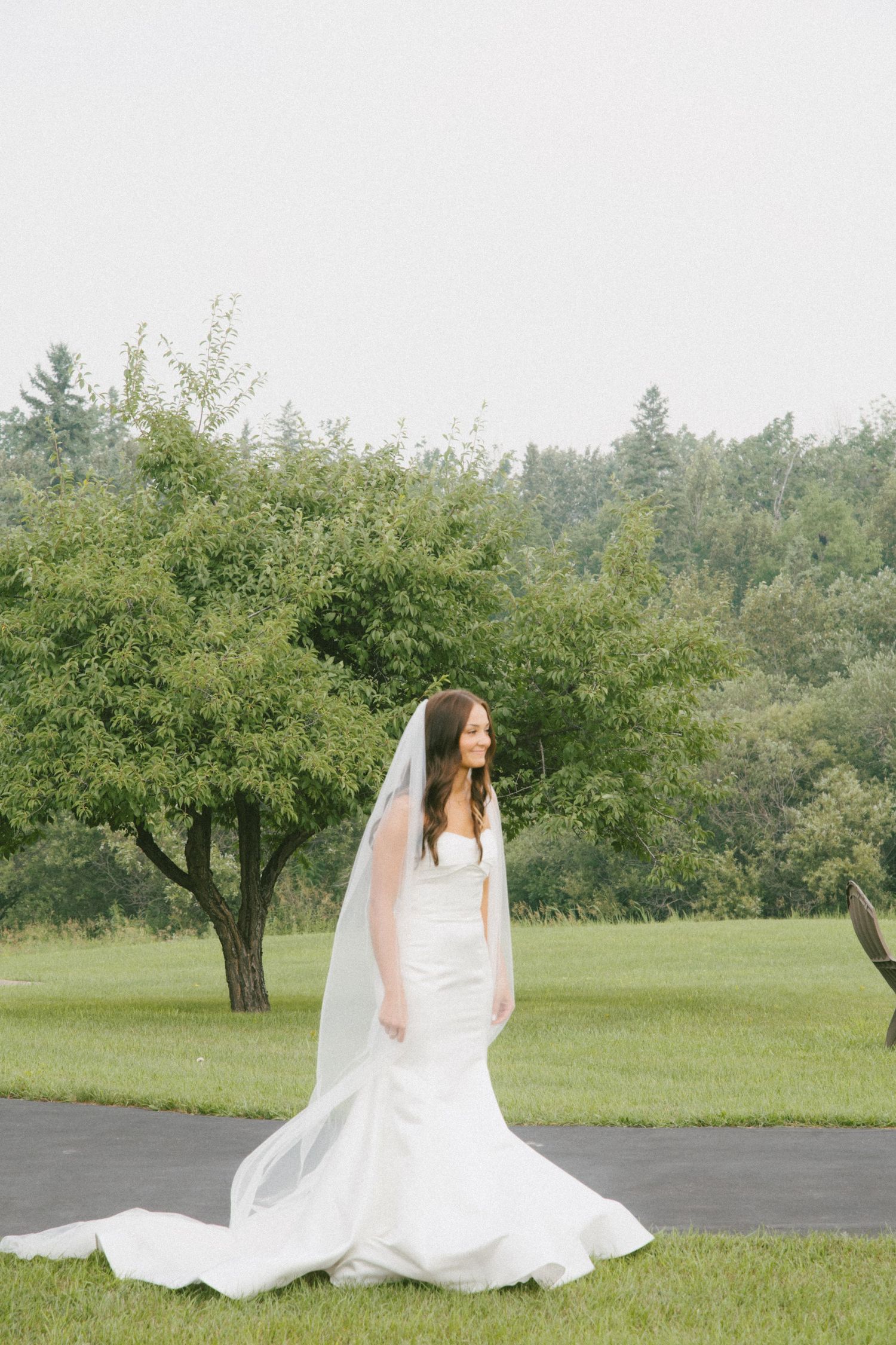 Bride in a fitted white mermaid gown and long veil standing on a path outdoors.