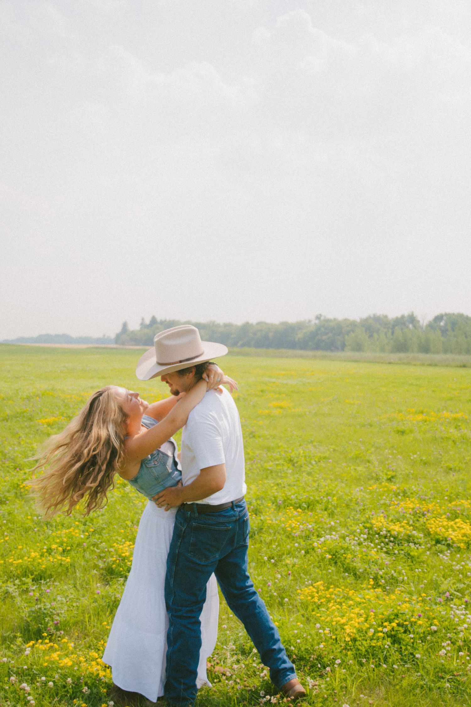 Couple dancing together in a blooming yellow wildflower field with the man wearing a cowboy hat.