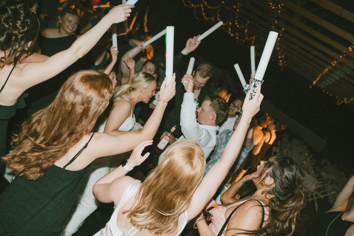 Guests dancing and holding white glow sticks at a lively wedding reception party.