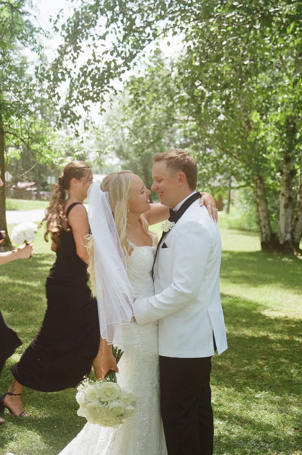 Bride and groom share a romantic moment outdoors, with bride in white gown and veil, groom in white tuxedo jacket.