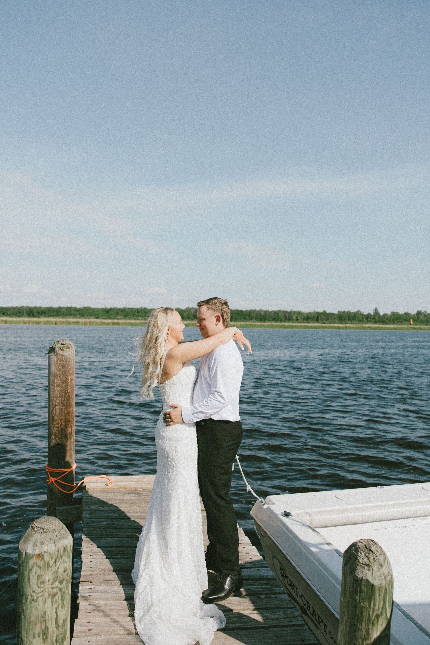 Bride and groom embracing on a wooden dock by a serene lake on their wedding day.