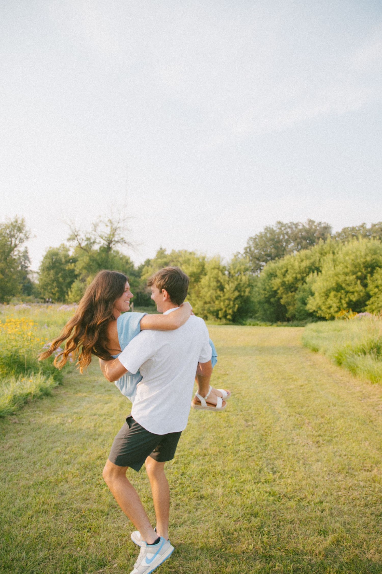 Man lifting woman in his arms while spinning in a sunny green outdoor field.