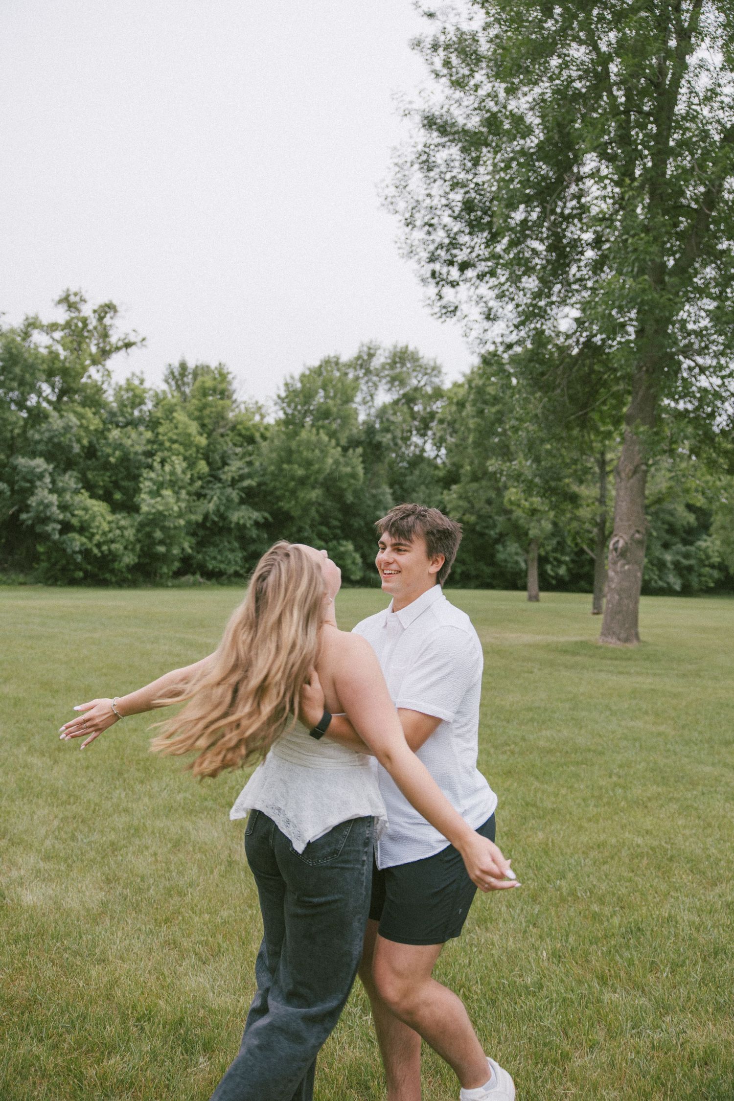 A joyful couple dancing together in a lush green park, the woman's hair flowing as they spin and smile.
