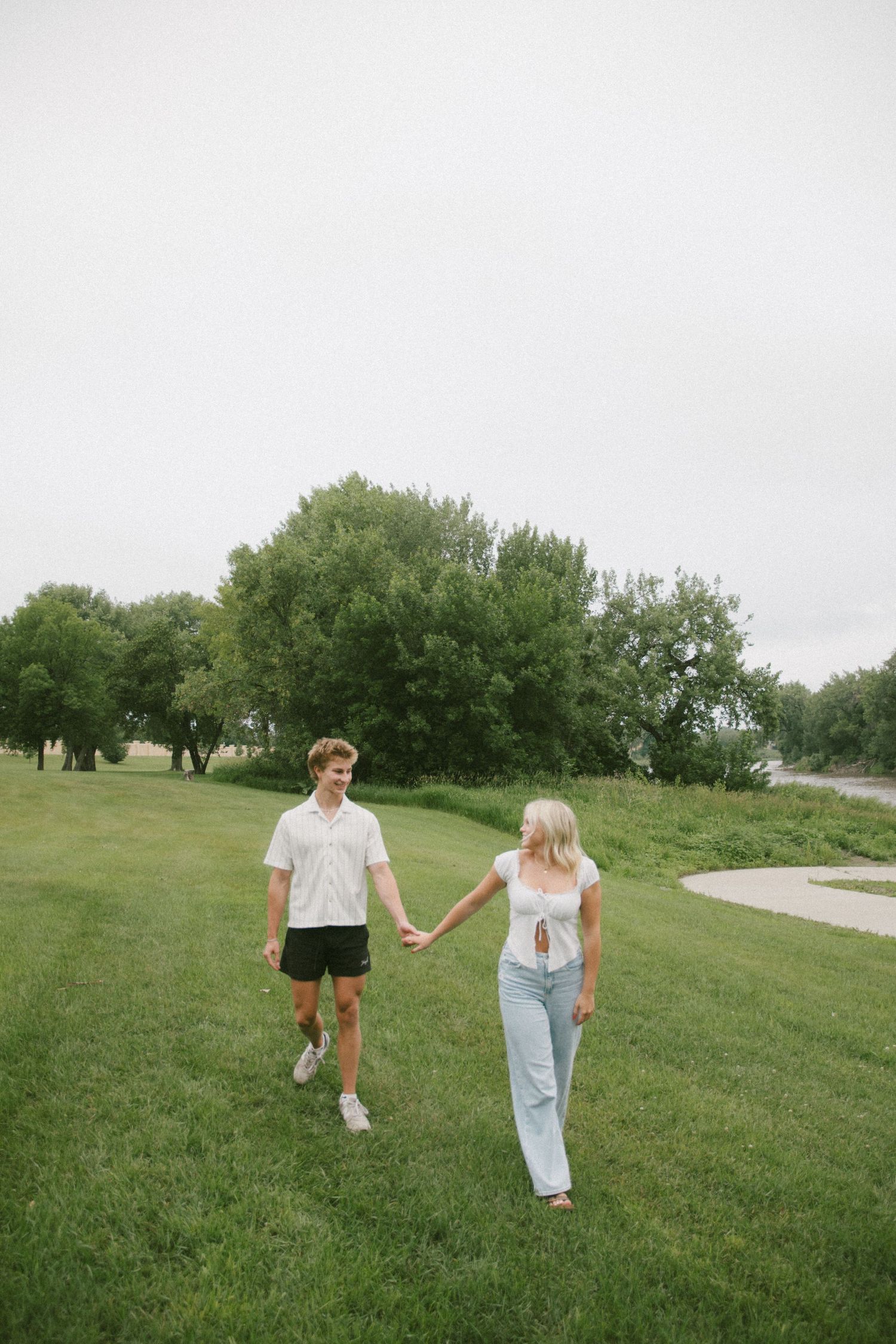 Couple walking hand in hand across a green grassy field with trees in the background.