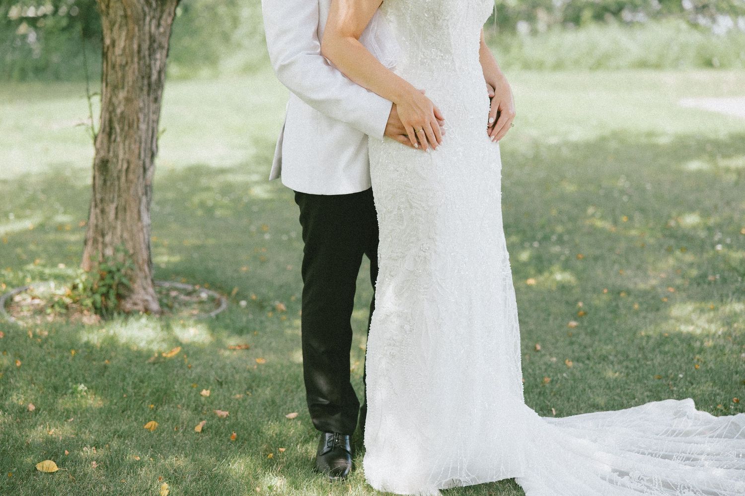 Bride and groom embracing outdoors in a lush green garden, wearing elegant white wedding gown and white suit.