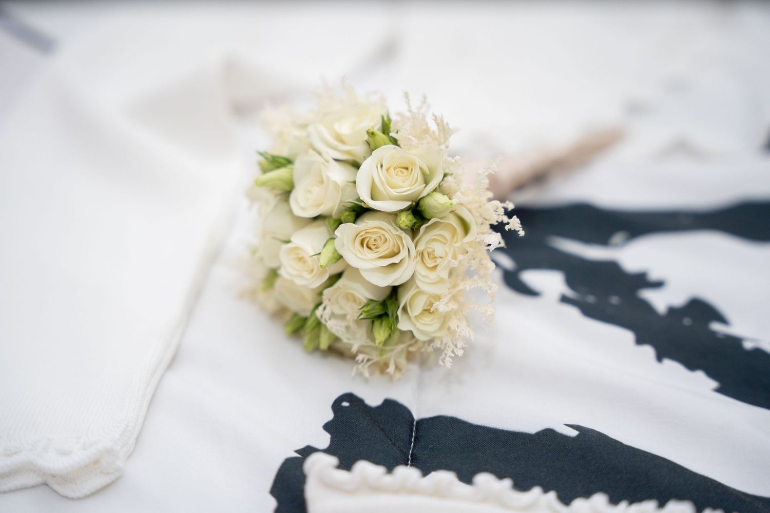 White rose bridal bouquet resting on a wedding dress with black lace detail.