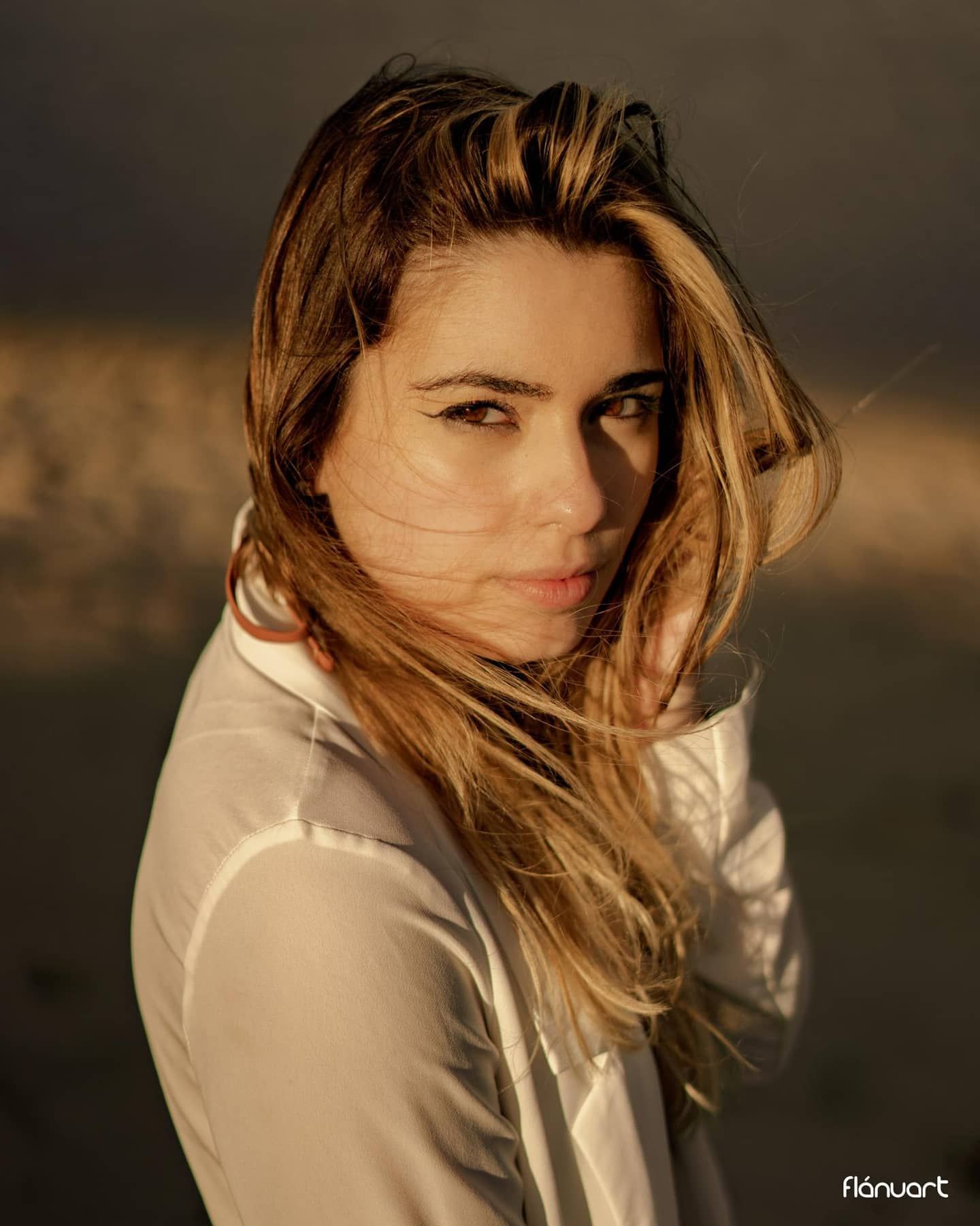 Woman with windswept blonde hair in white shirt during golden hour outdoor portrait.