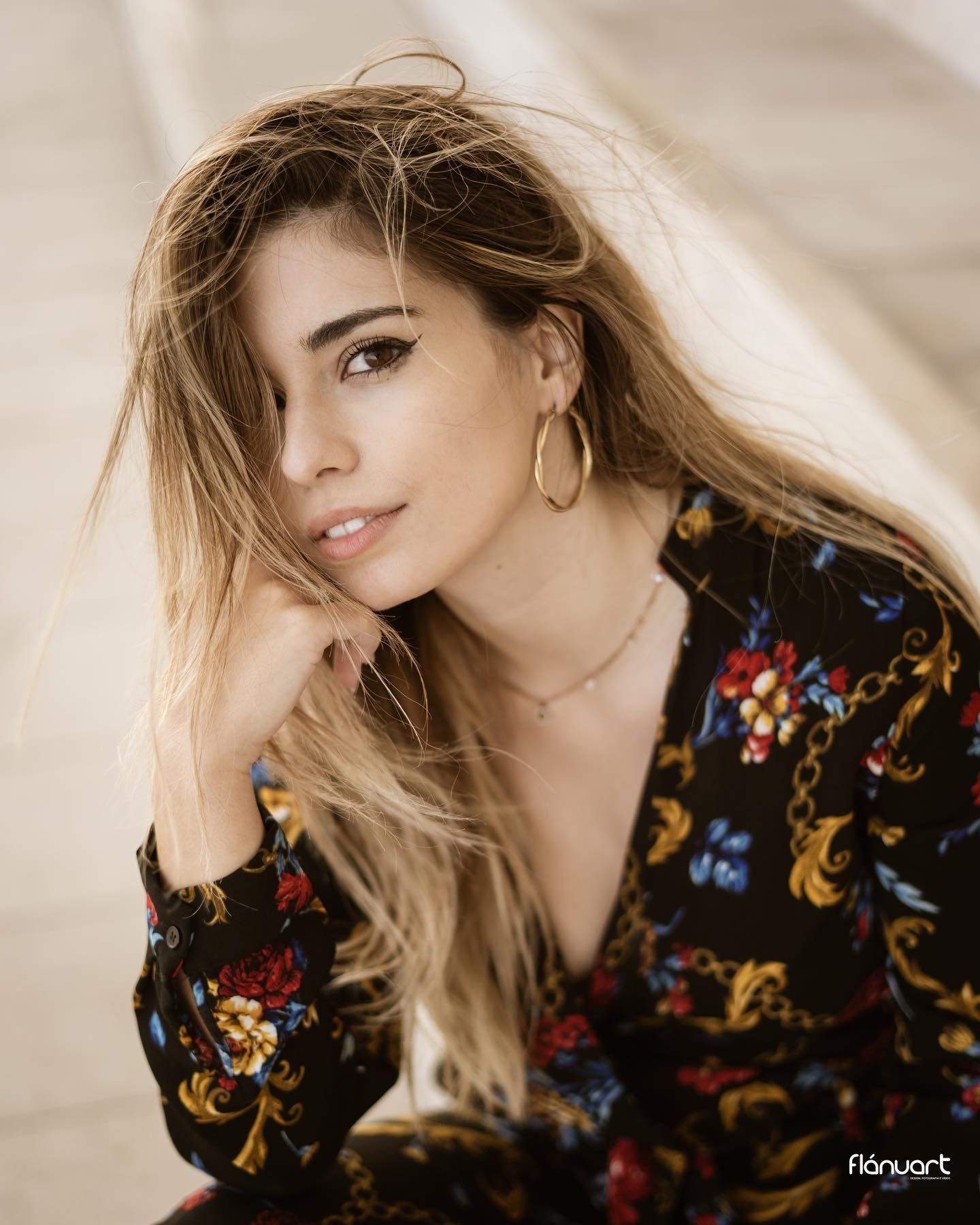 Close-up portrait of blonde woman in floral dress with hoop earrings and necklace.
