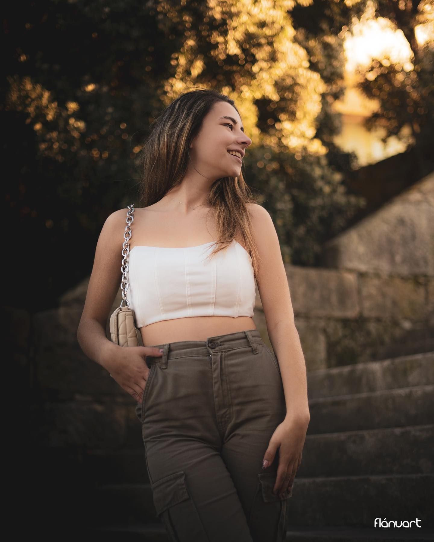 Smiling young woman in white crop top and olive pants posing outdoors at golden hour.