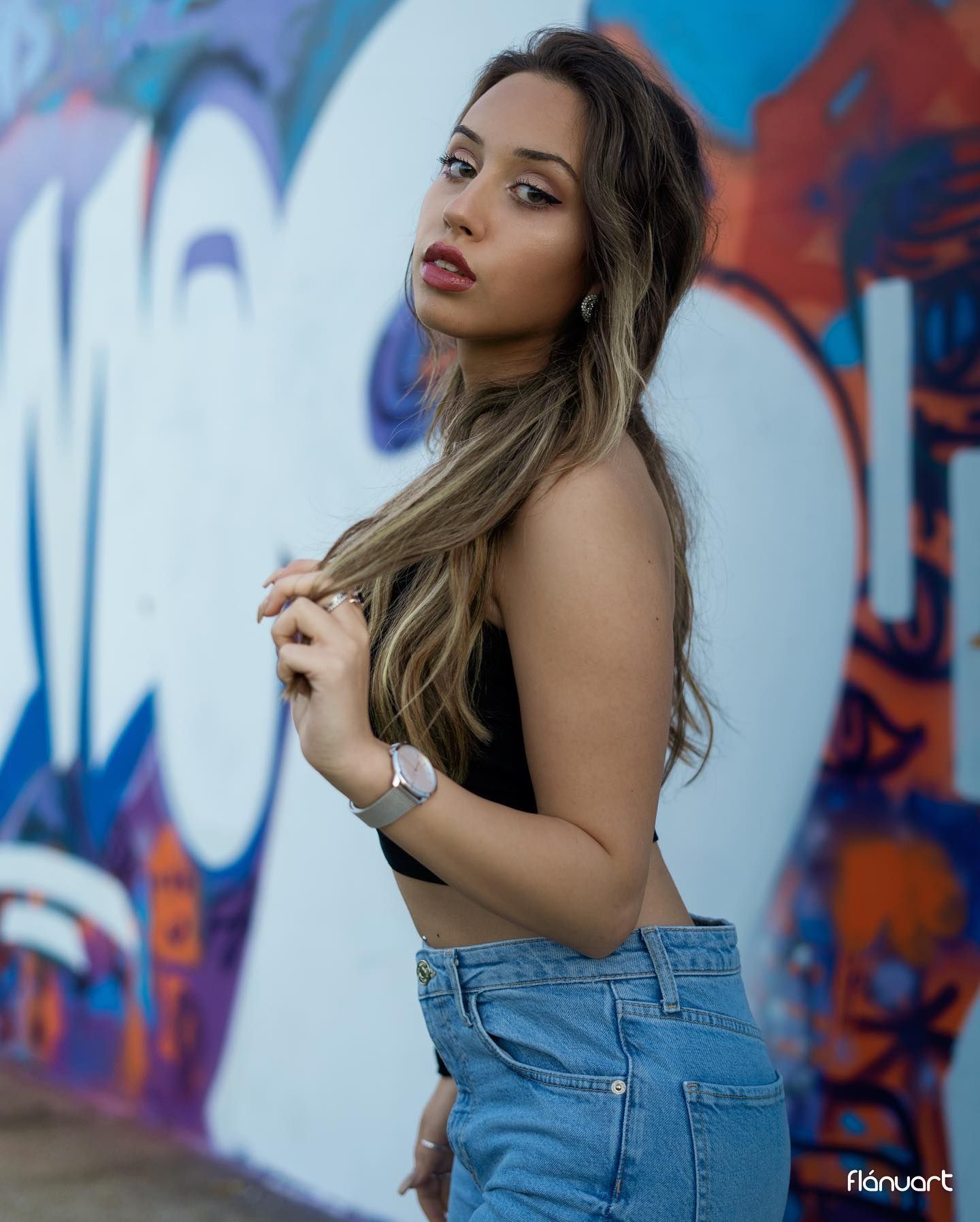 Stylish woman in black crop top and high-waisted jeans posing confidently against a colorful graffiti wall.
