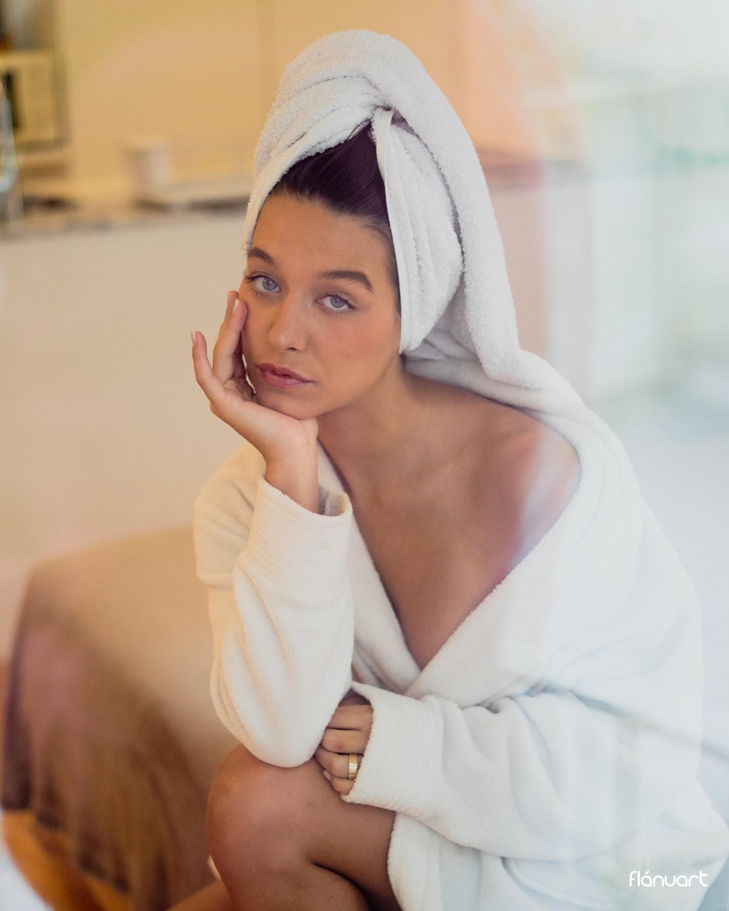 Woman in white bathrobe with a towel on her head in a soft bathroom setting.