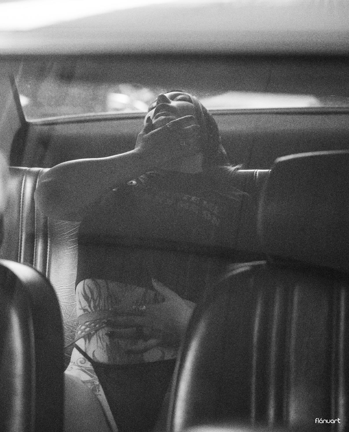 Black and white photo of a person relaxing across the backseat of a vintage car interior.