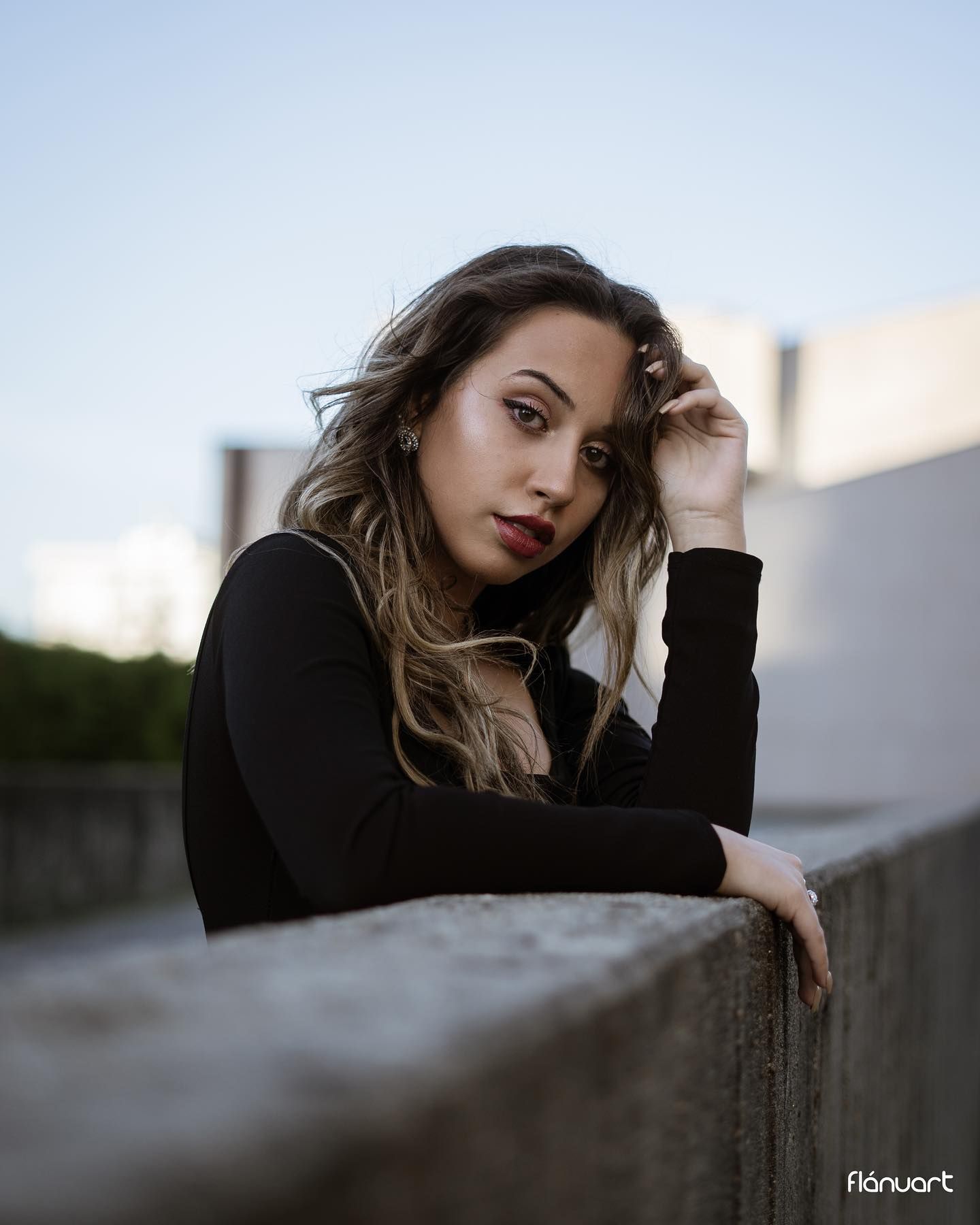 Young woman in black turtleneck leaning on a concrete wall outdoors at dusk.