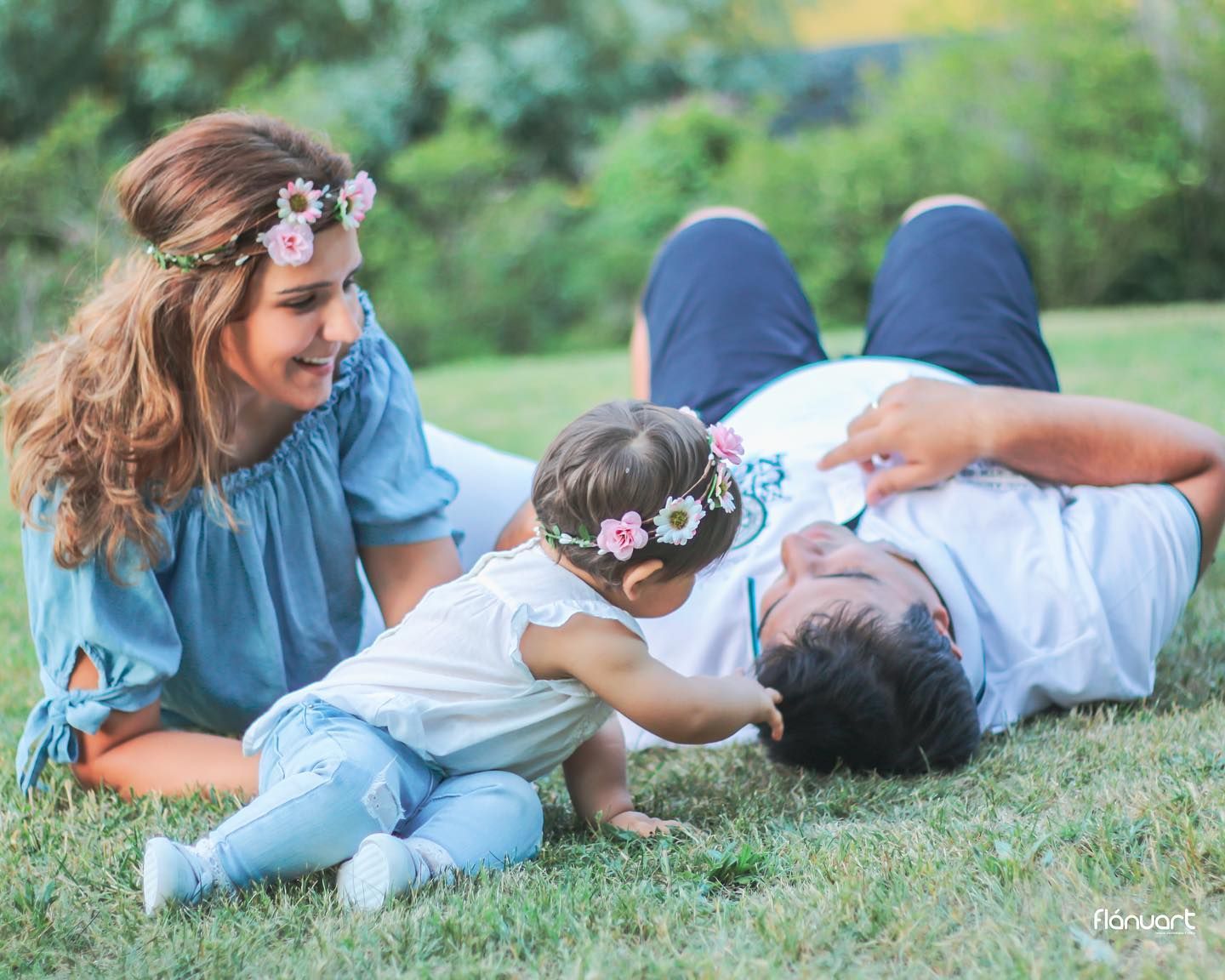Happy family with mother, father, and baby girl relaxing together on green grass in park.
