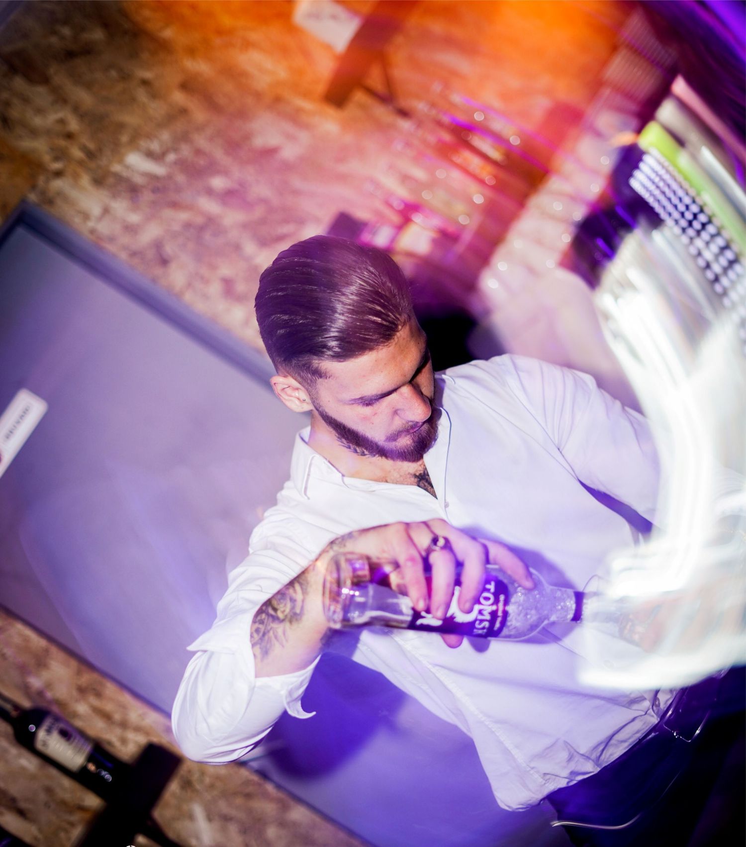 Tattooed male bartender in white shirt mixing cocktails at a nightclub.