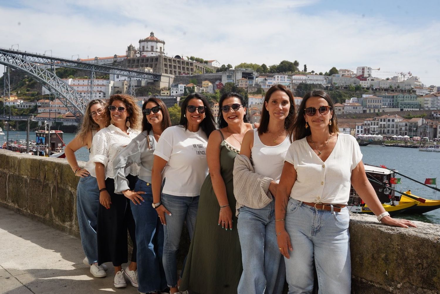 A group of seven women in white tops posing together with Porto's Dom Luis bridge in the background.