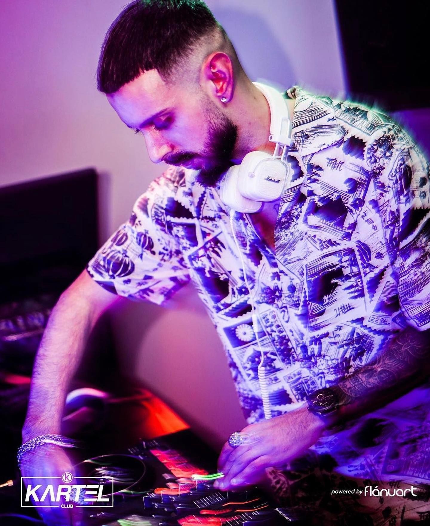 Bearded DJ with headphones around neck mixing tracks at Kartel Club nightclub event.