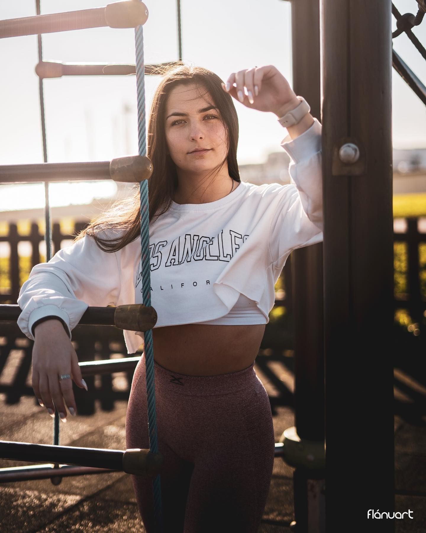 Young woman in Los Angeles crop sweatshirt and leggings poses at outdoor gym at golden hour.