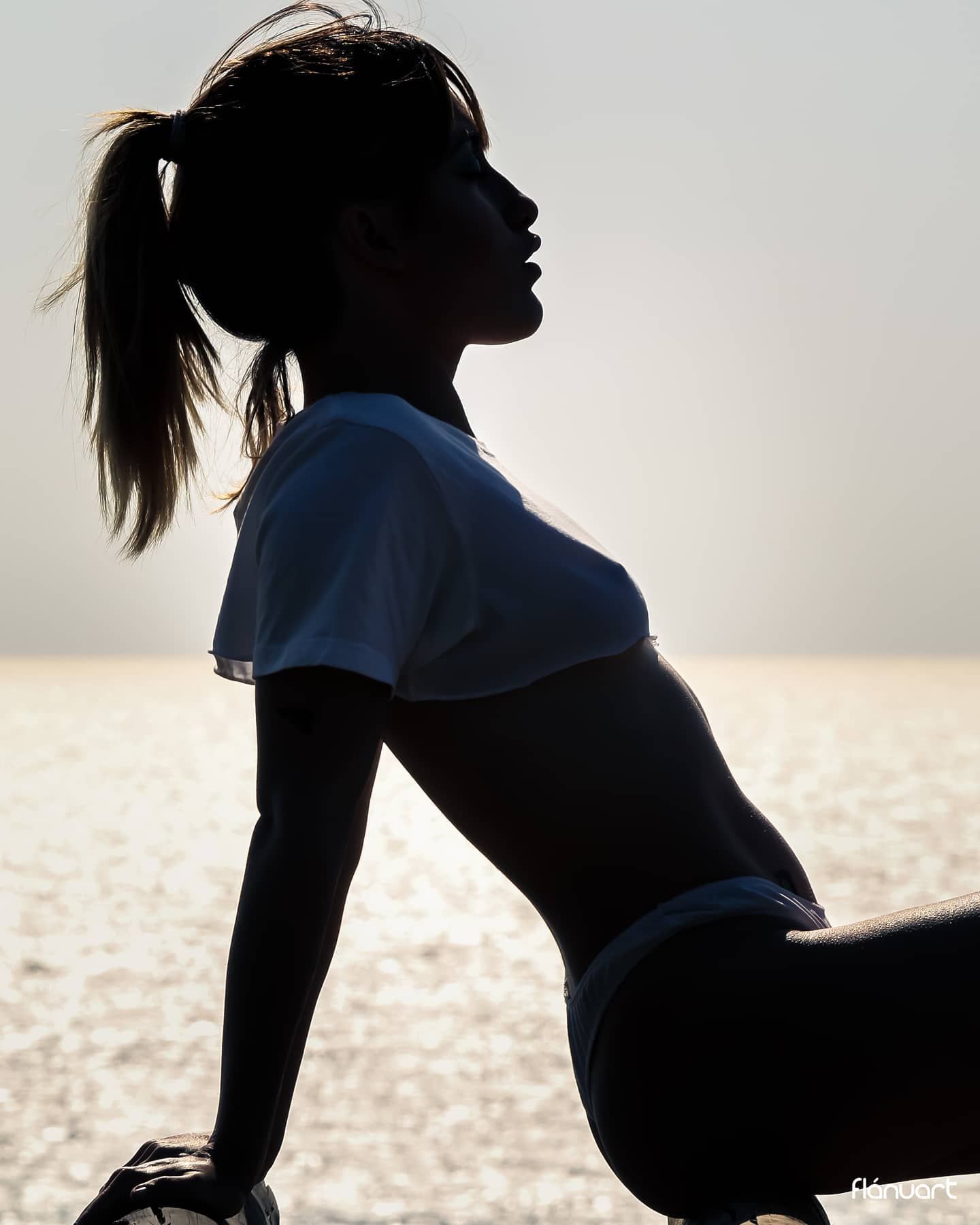 Silhouette of woman in athletic wear posing against bright ocean background.