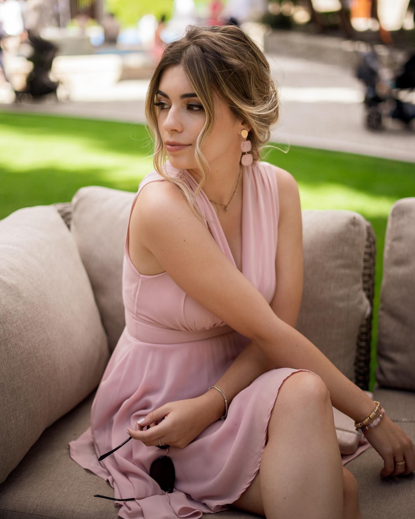 Elegant young woman in pink halter dress sitting on outdoor sofa with updo hairstyle.