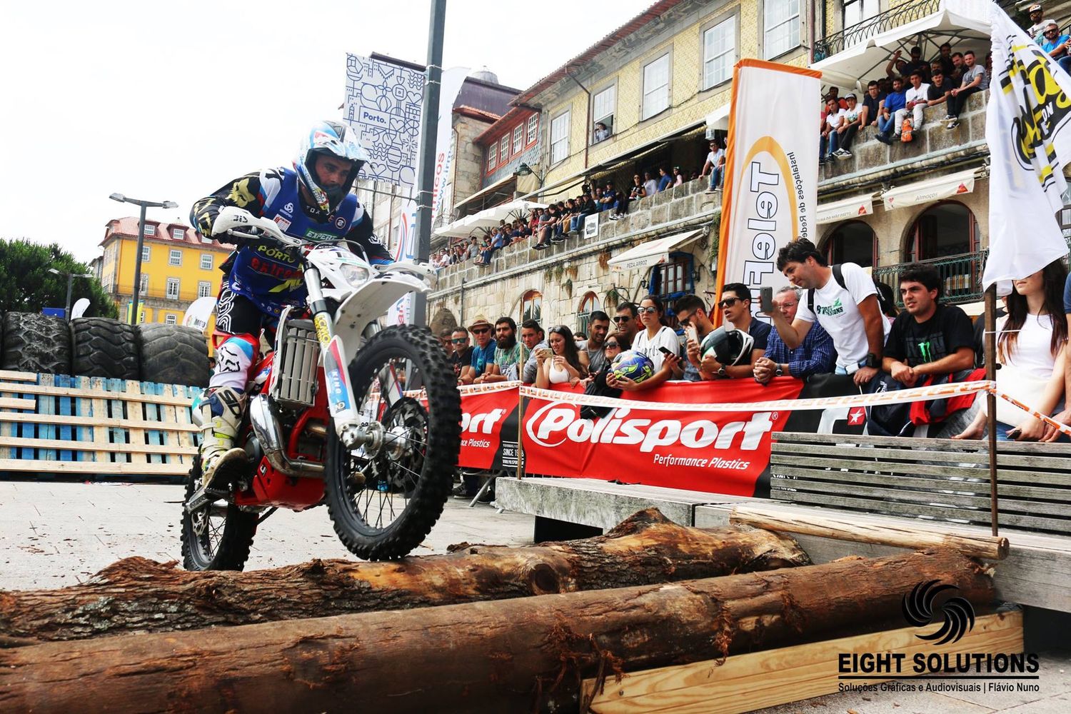 Motocross rider performing a stunt over logs at a Polisport-sponsored urban trial event.