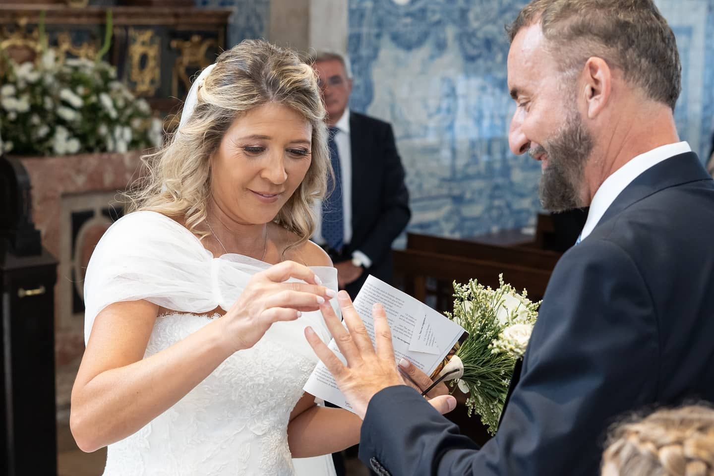 Bride reading vows while groom attentively listens during intimate church wedding ceremony with blue tiles.