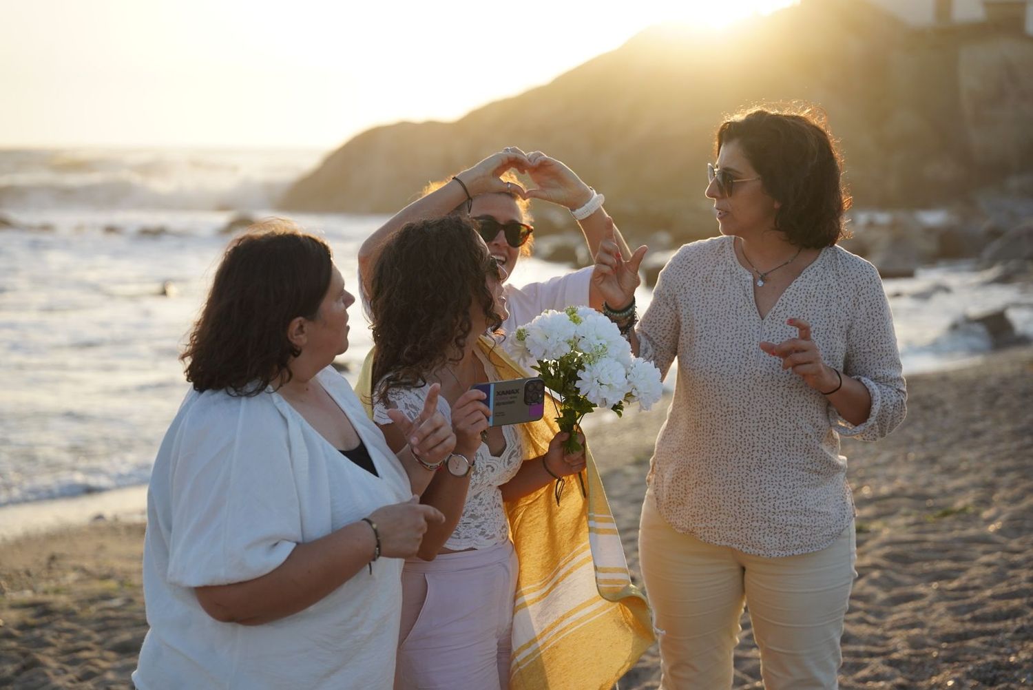 A joyful group of women dancing and celebrating on a sandy beach during a warm golden sunset.
