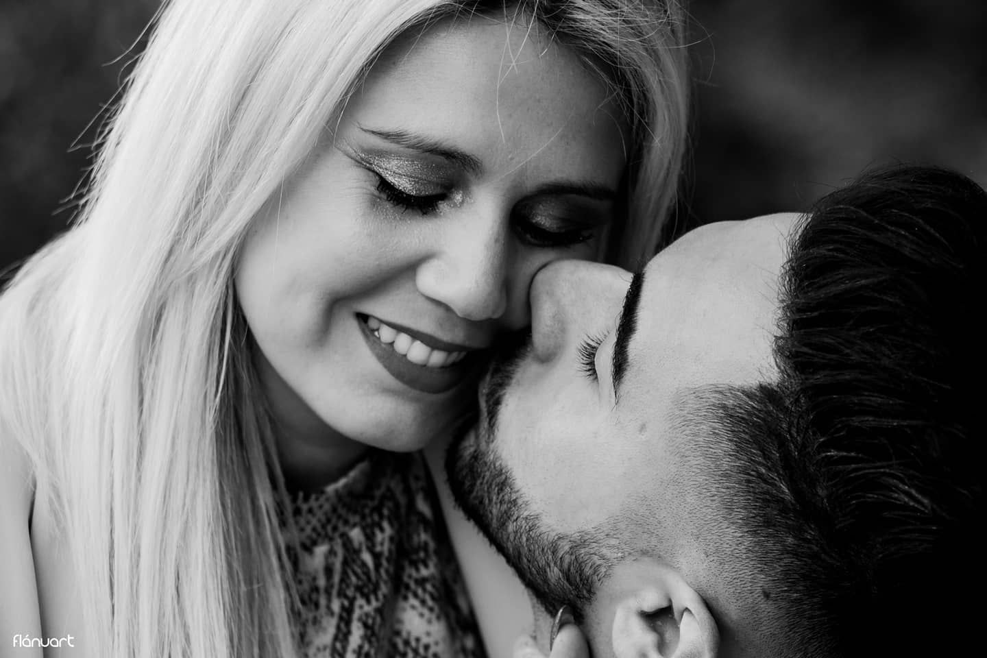Black and white romantic close-up of smiling blonde woman and bearded man sharing a tender moment.