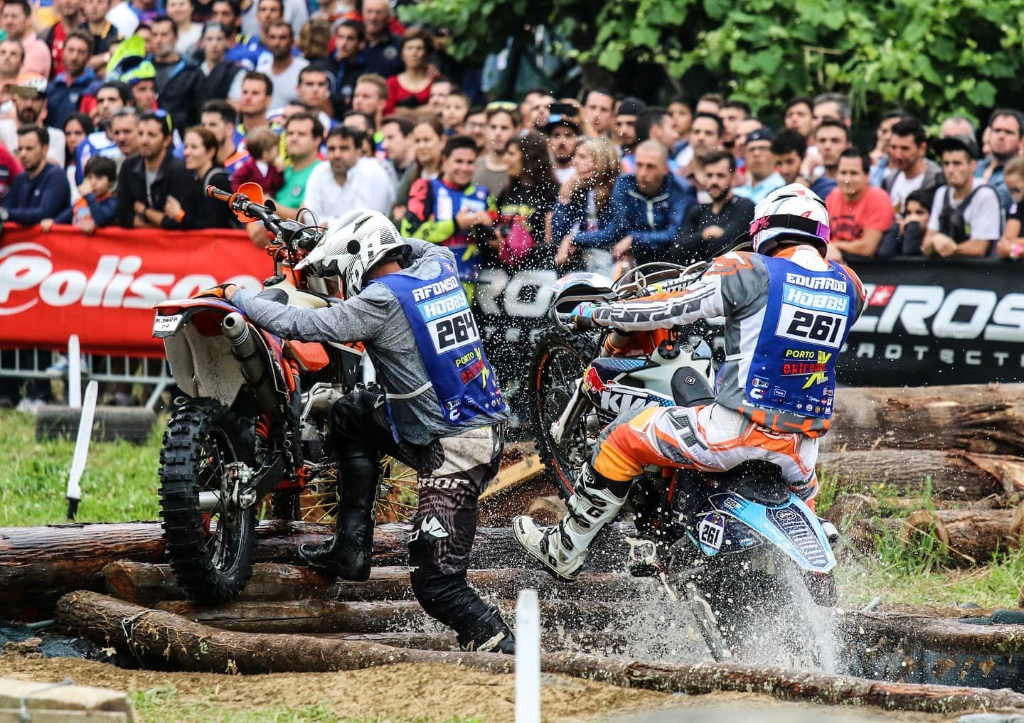 Two motocross riders colliding on a muddy off-road trail during a competitive race event.
