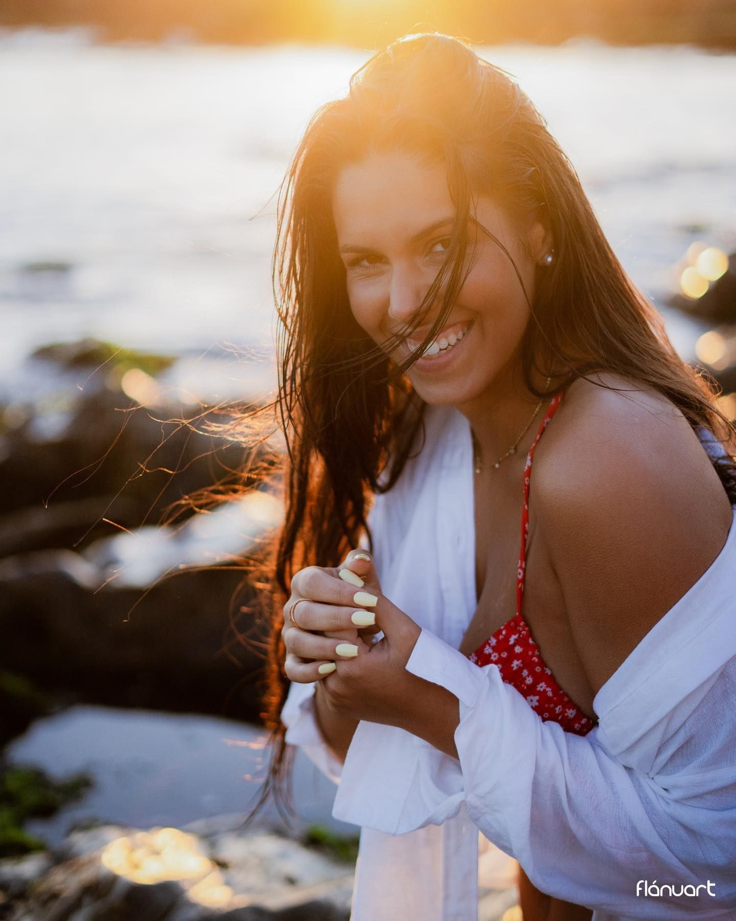 Woman smiling in white shirt and red bikini top during stunning beach sunset.