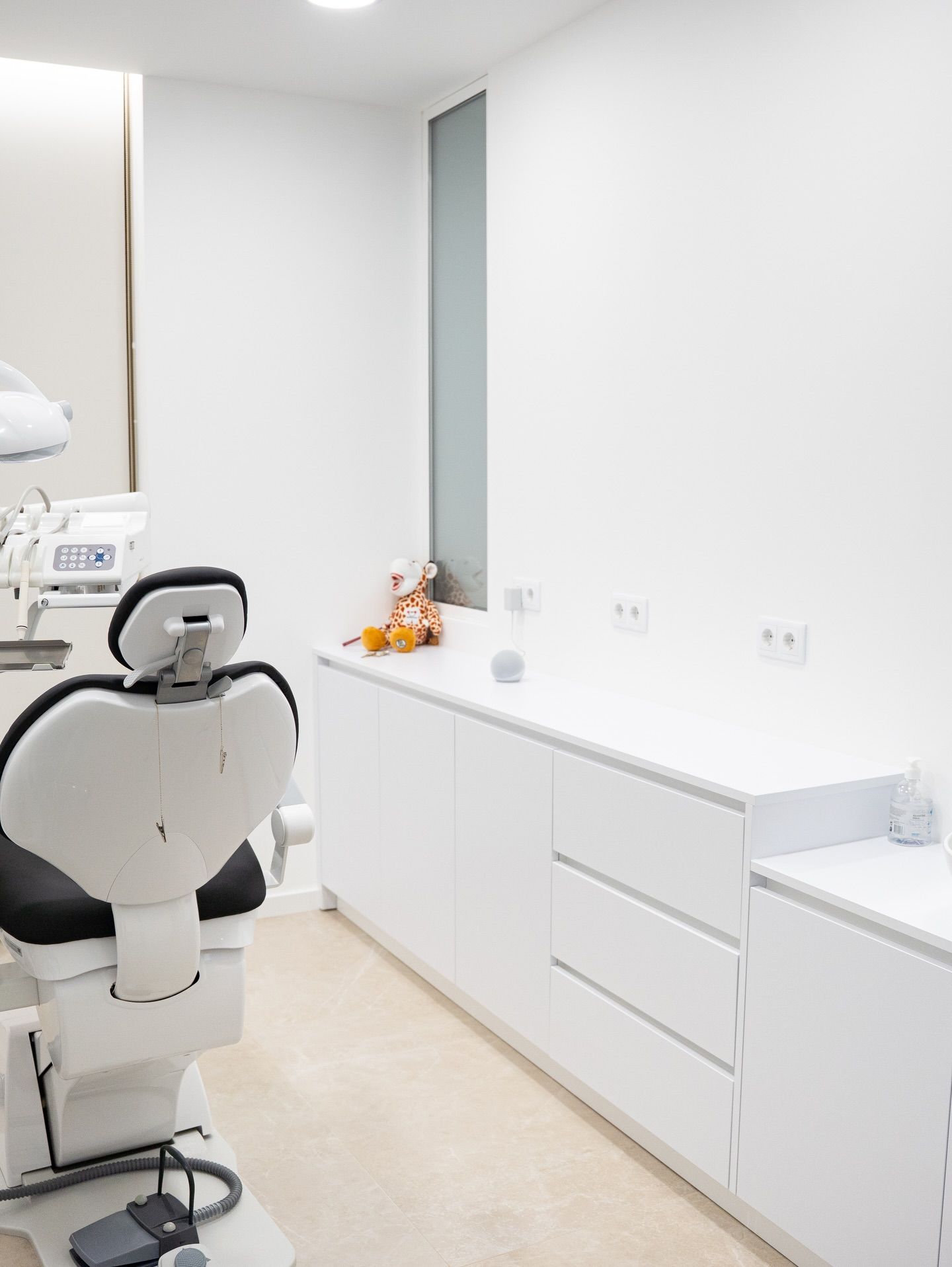 Clean minimalist dental office with black treatment chair and white cabinetry storage unit.