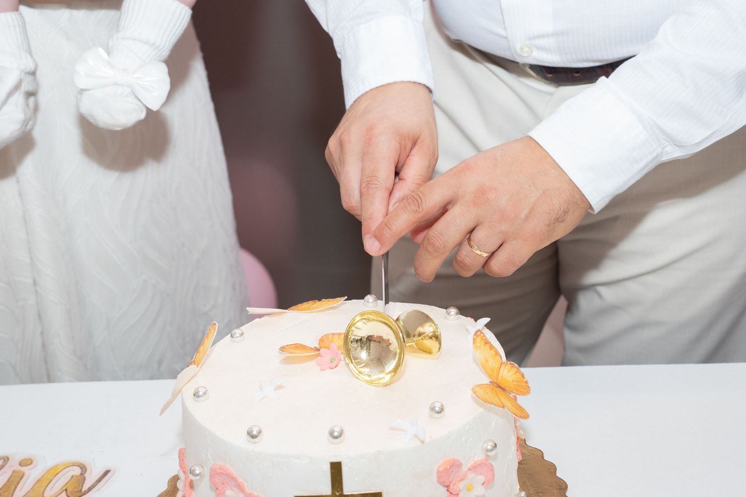 Couple cutting a white wedding cake decorated with gold rings and pink flowers at a wedding reception.