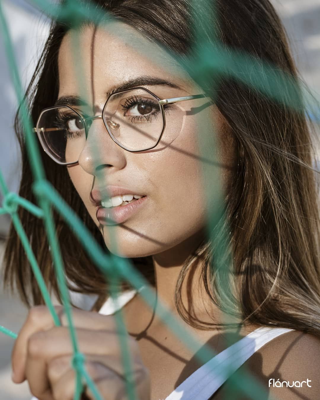Close-up portrait of brunette woman wearing round glasses viewed through green rope netting.