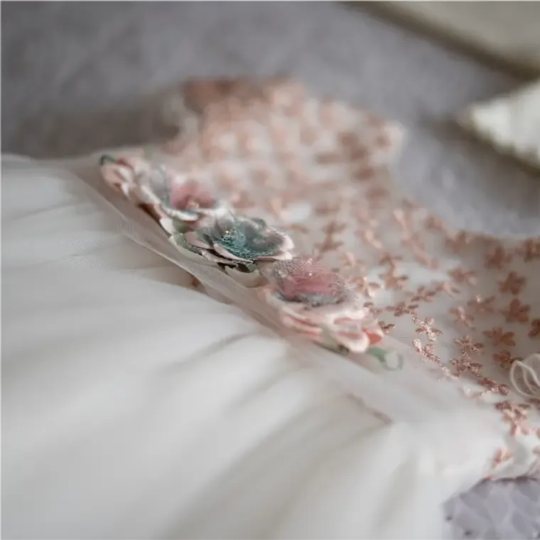 Close-up of delicate floral embroidery on a white fabric with pink and blue 3D flowers.