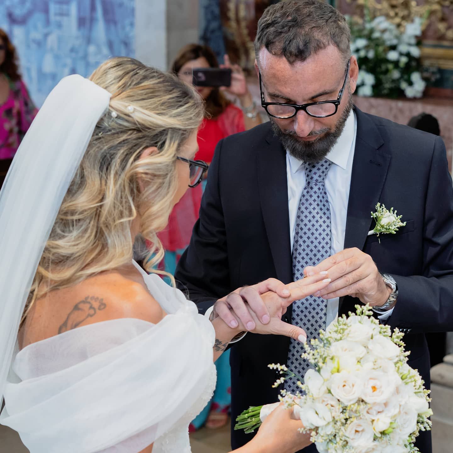 Groom places wedding ring on brides finger during an intimate church ceremony with guests watching.