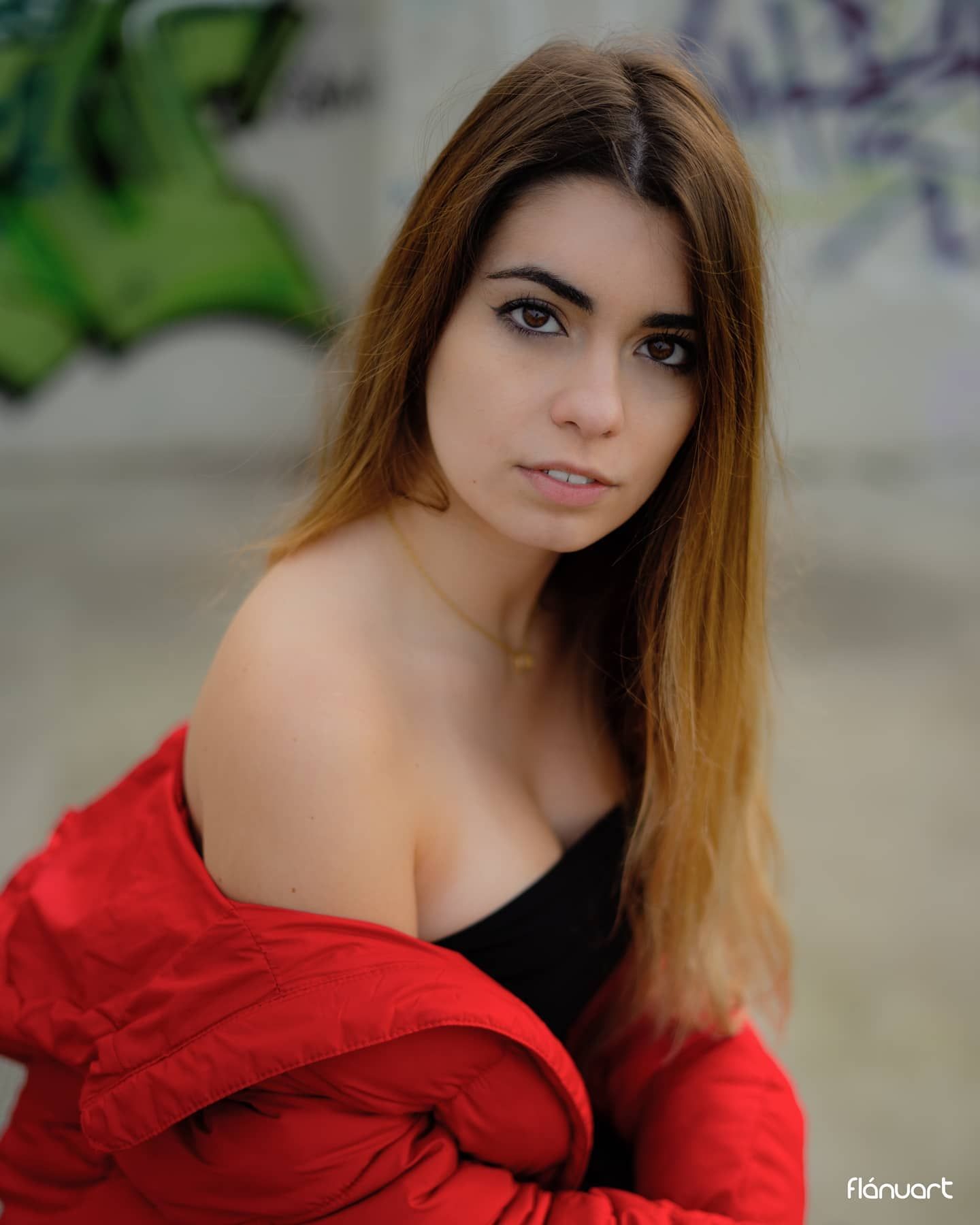 Young woman in red jacket and black top posing in front of a colorful graffiti wall.