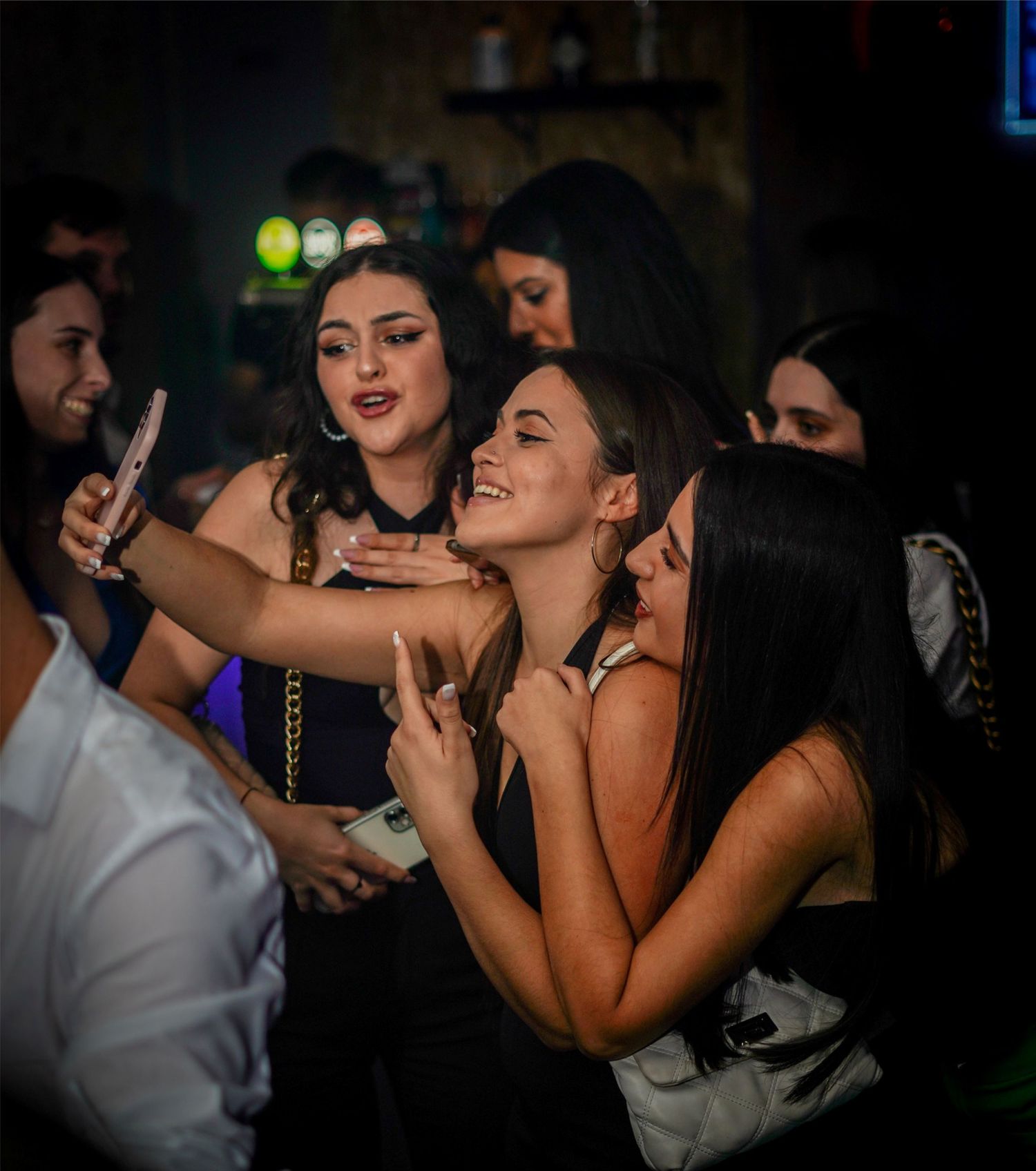 Group of young women taking a selfie at a nightclub party, smiling and making peace signs.