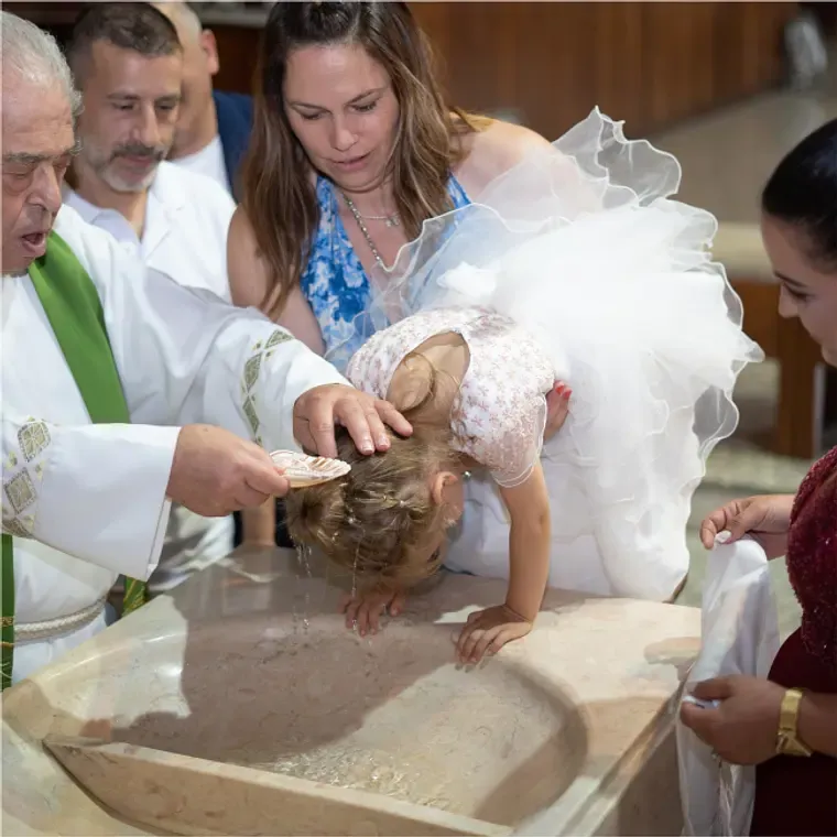 Priest performing baptism on a young girl at a church font during ceremony.