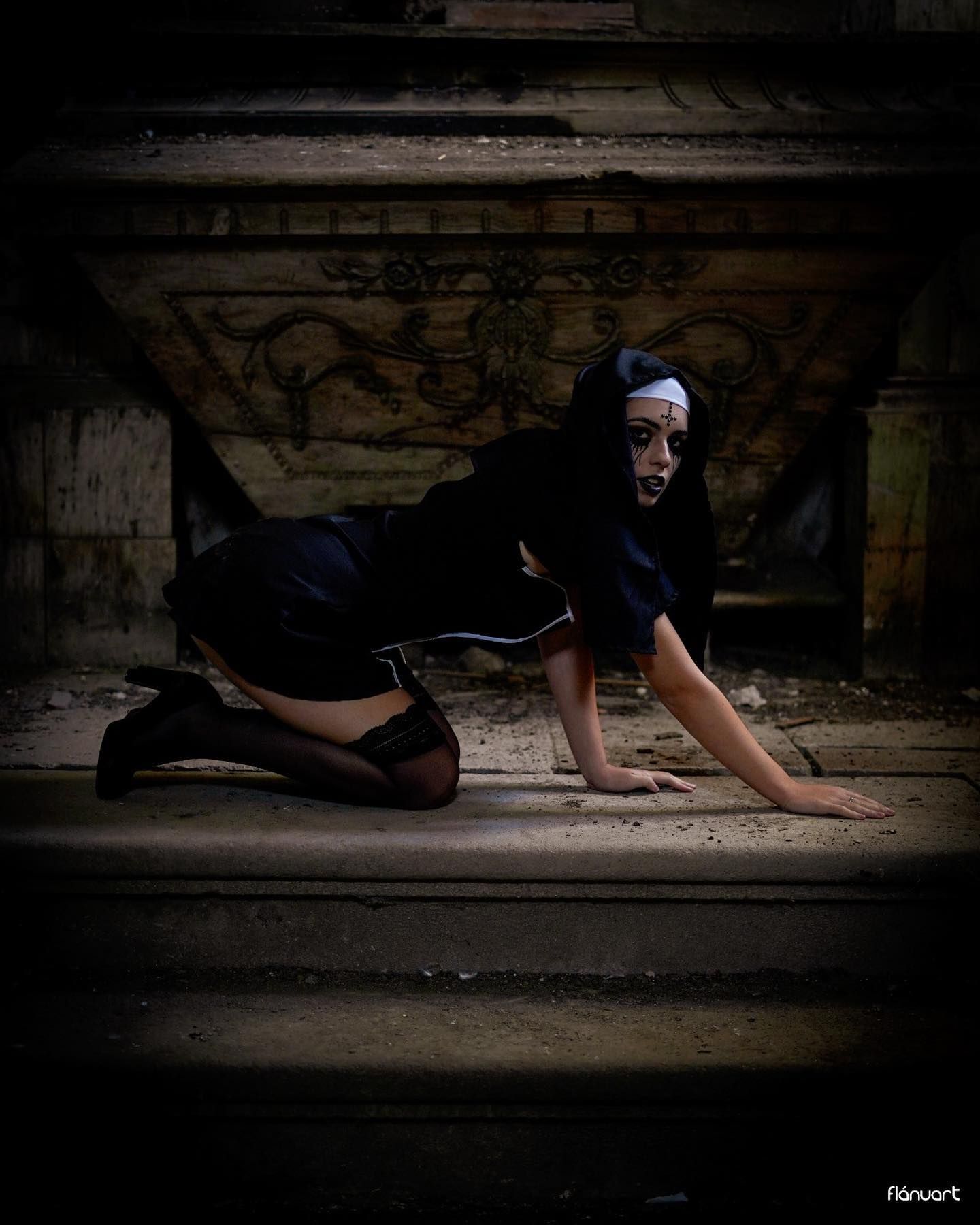 Woman in nun costume crawling on floor of abandoned building with graffiti walls.