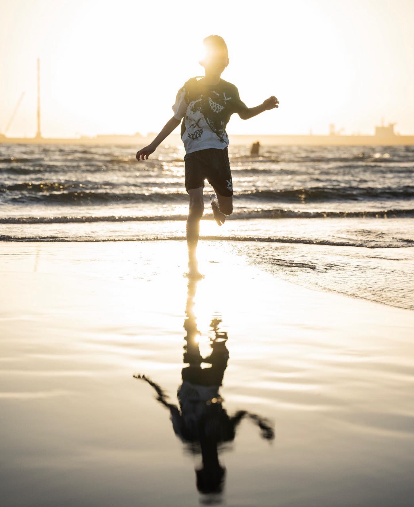 Person running along wet beach shoreline at golden sunset with reflection in water.