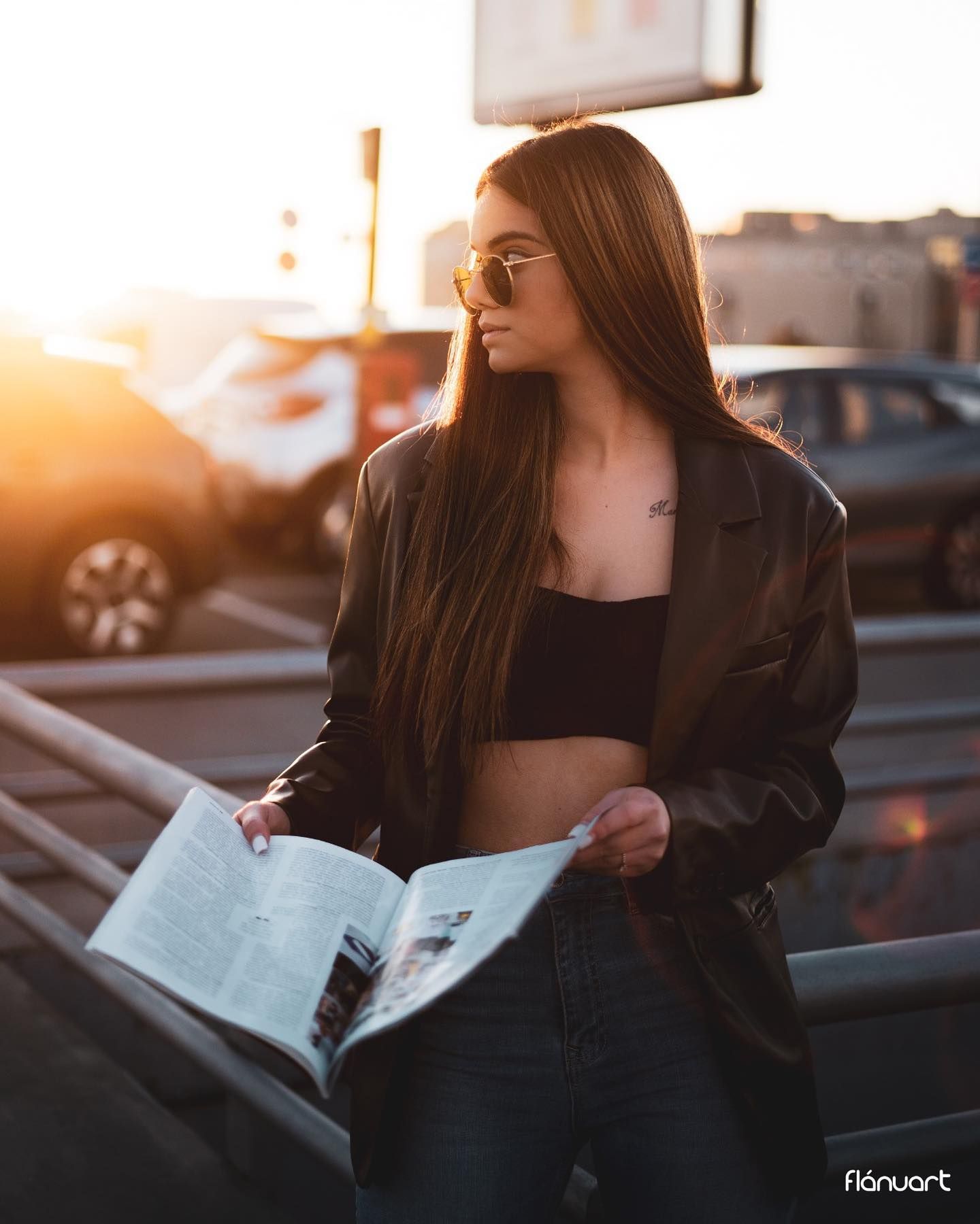 Woman in black crop top and blazer holding magazine at golden hour urban setting.