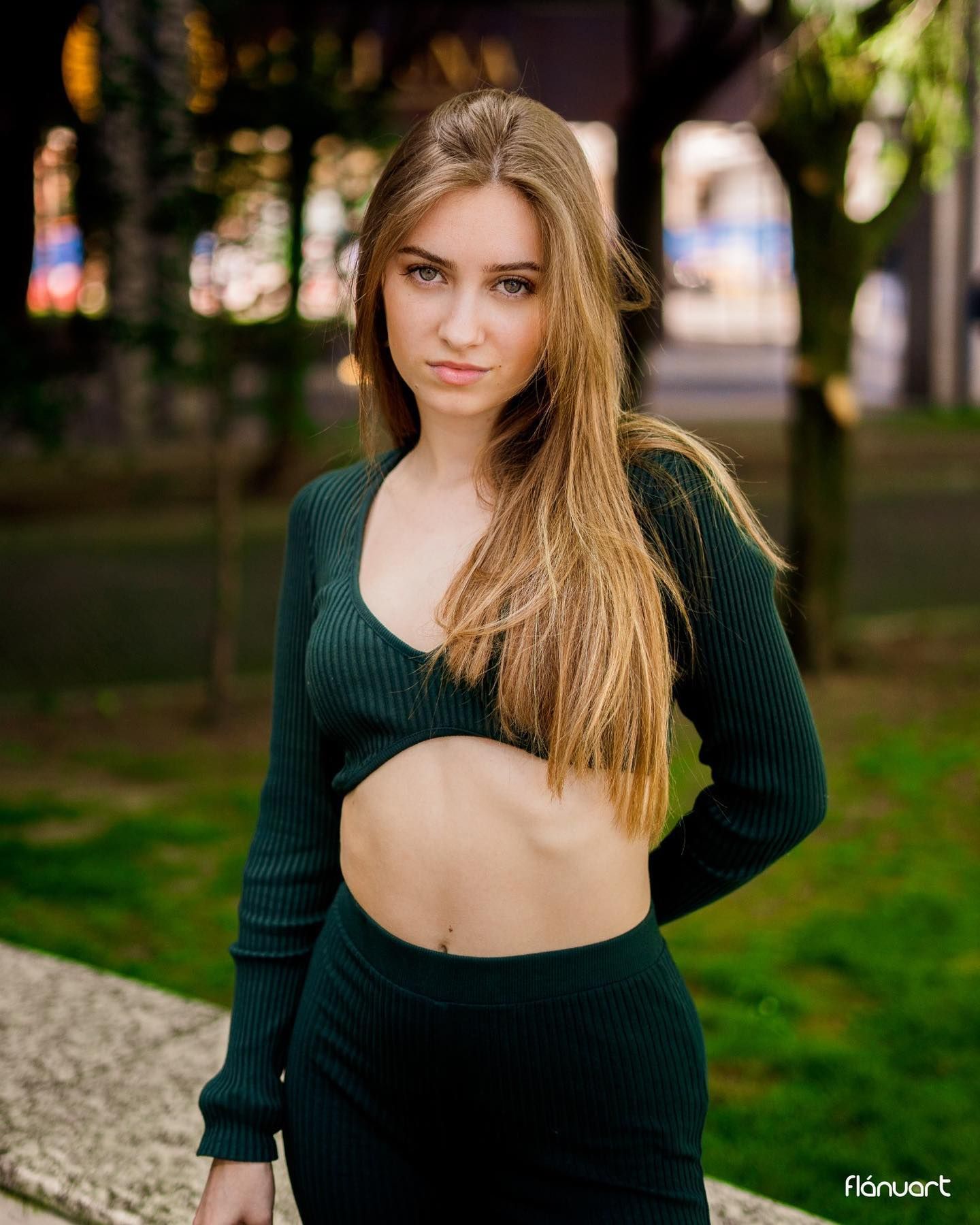 Blonde woman in a dark green cutout knit co-ord set posing in an urban park at dusk.