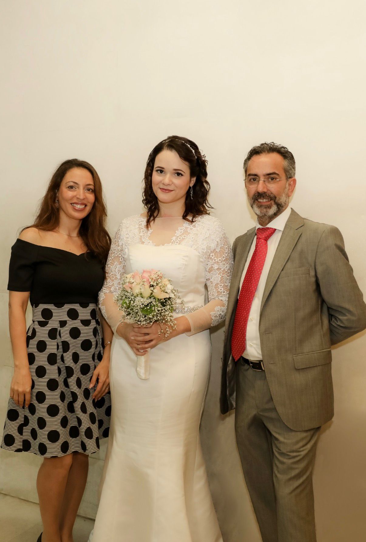 Bride in lace gown holding pink bouquet poses with two guests at elegant indoor wedding venue.